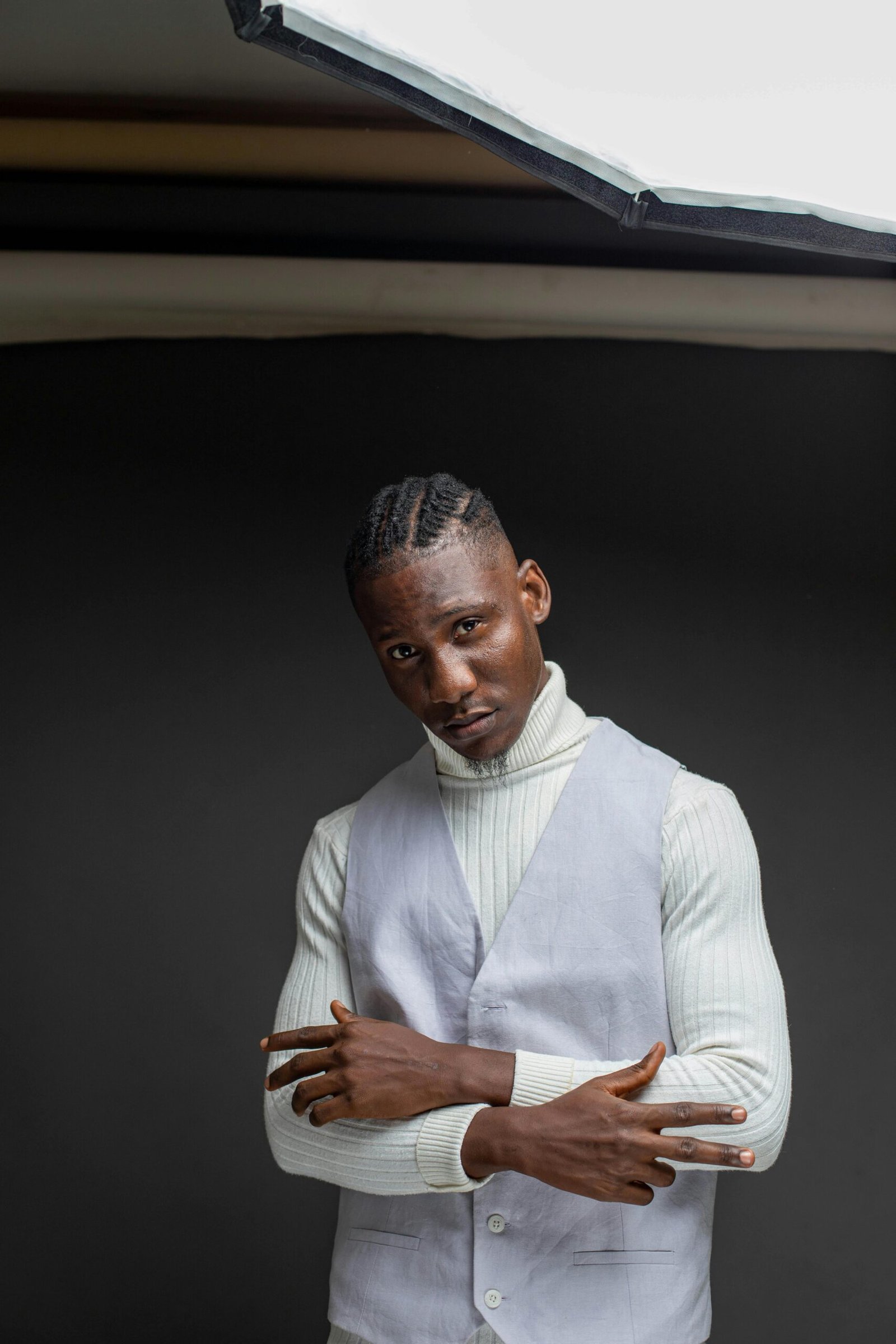 Studio portrait of an adult man in a turtleneck sweater with crossed arms against a dark background.